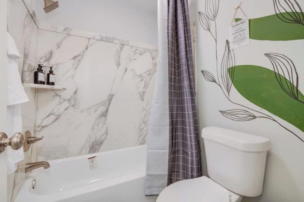 A bathroom with a marble wall, a white bathtub, a toilet, and a shower curtain.