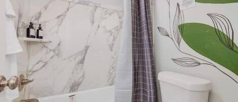 A bathroom with a marble wall, a white bathtub, a toilet, and a shower curtain.