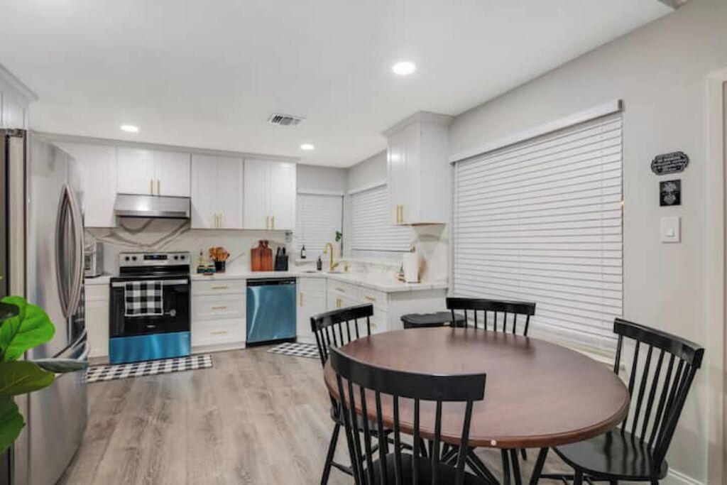 Una cocina moderna con armarios blancos, un refrigerador azul y un comedor con una mesa redonda y sillas.