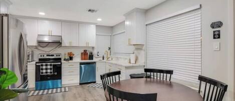 Una cocina moderna con armarios blancos, un refrigerador azul y un comedor con una mesa redonda y sillas.