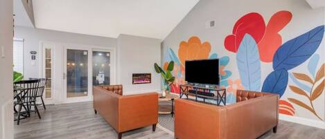 A living room with two leather sofas, a flat-screen TV, and a colorful wall mural.