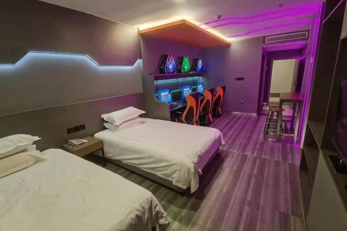 Ein modernes Hotelzimmer mit zwei Betten, einem Schreibtisch mit Computer und einer Sitzecke mit Sesseln.