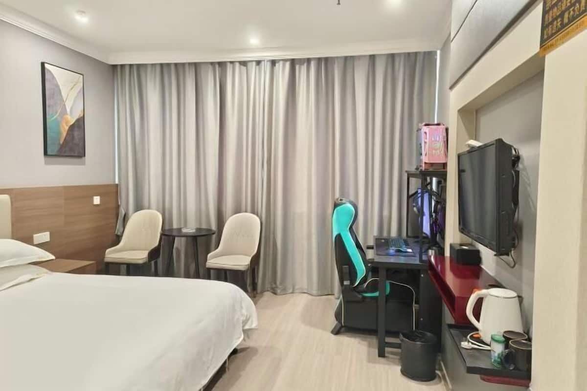 Ein Hotelzimmer mit einem Bett, zwei Stühlen, einem Schreibtisch mit Computer, einem Fernseher und einer Kaffeemaschine.