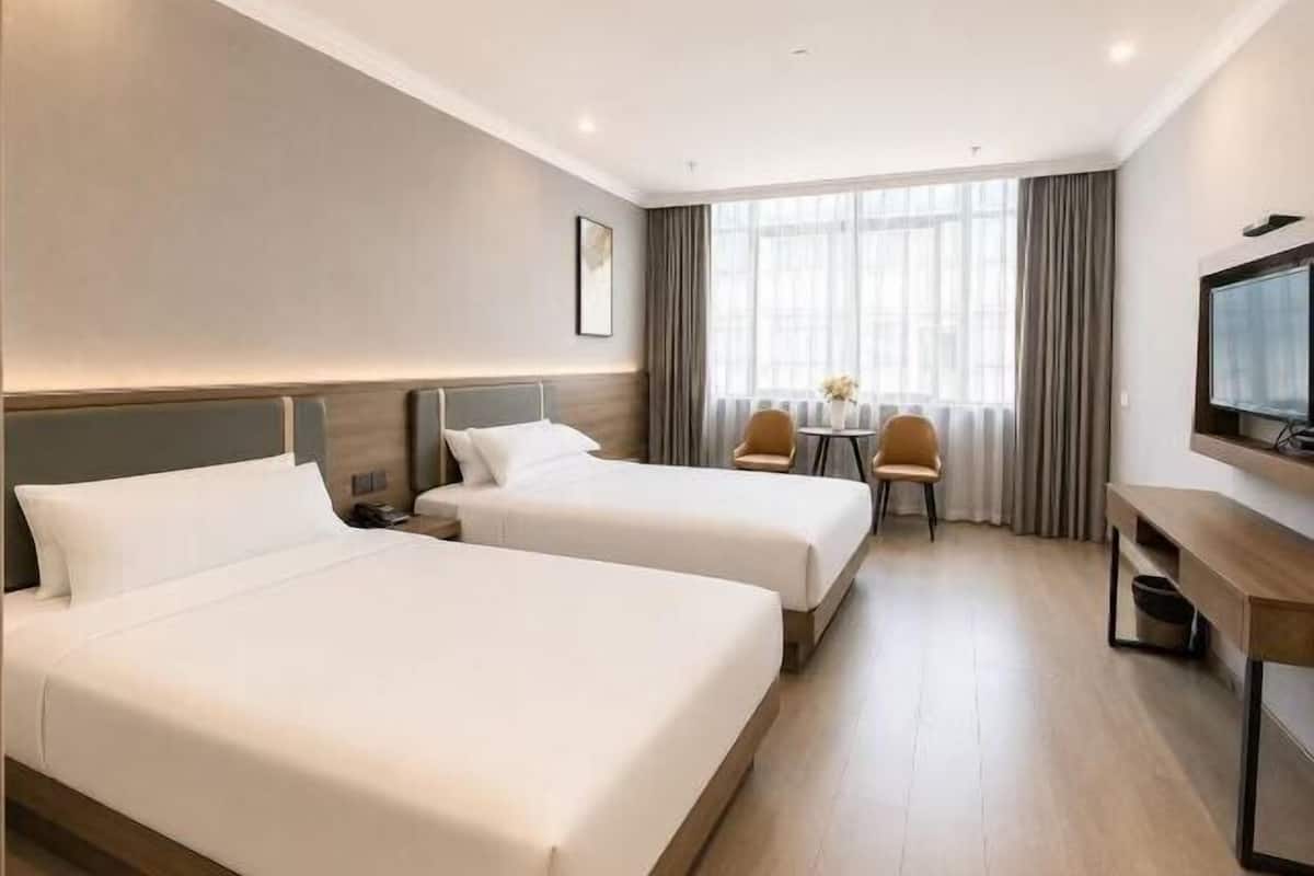 Ein Hotelzimmer mit zwei Betten, einem Schreibtisch, einem Stuhl, einem Fernseher und einem Fenster mit Vorhängen.