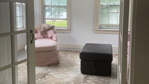 Ein Zimmer mit großem Fenster, einem Bett, einem Sessel und einem Stauraum-Pouff.