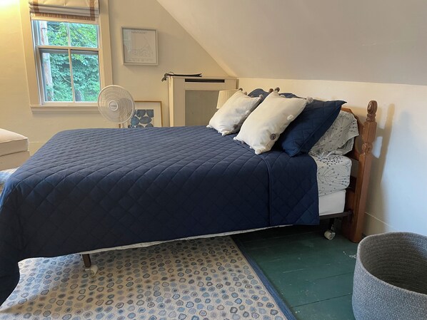 Un dormitorio con cama, almohadas, cabecera de madera, ventana, ventilador y alfombra.
