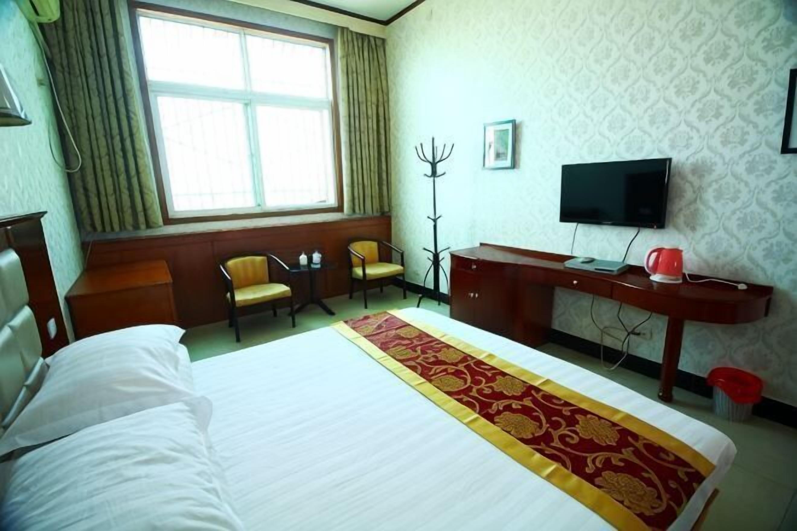 A hotel room with a bed, two chairs, a desk, a television, and a window with curtains.