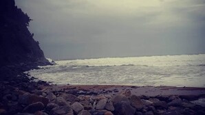 Une plage rocheuse où les vagues s’écrasent sur le rivage sous un ciel nuageux.