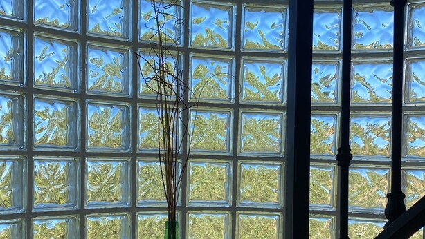 Un escalier doté d’une balustrade en verre et d’un vase vert orné de branches, le tout posé sur un sol carrelé.