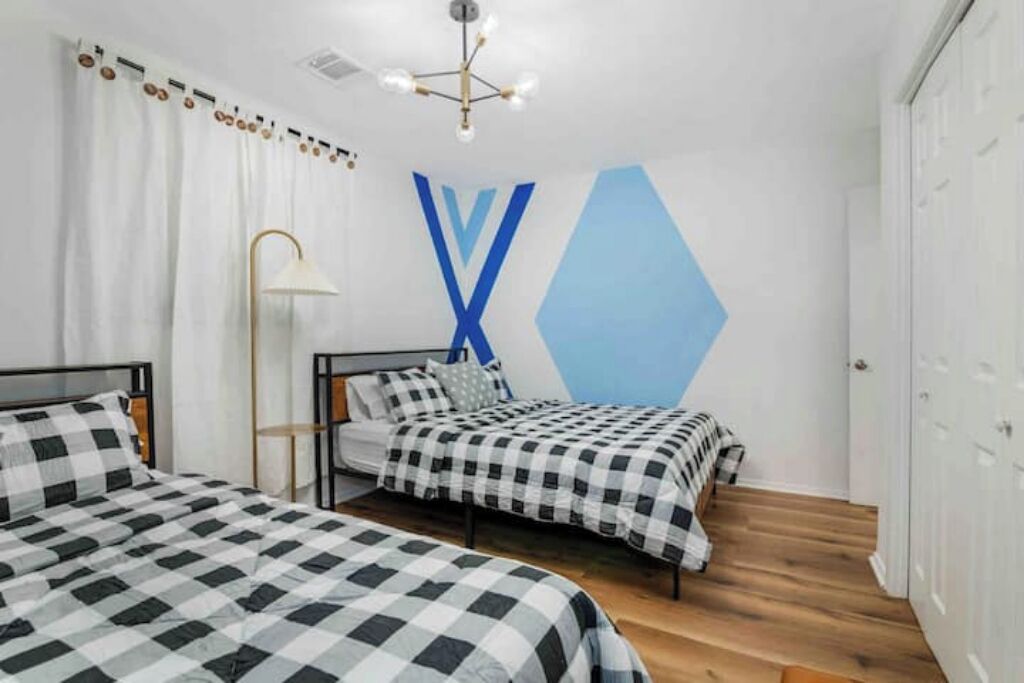 Een slaapkamer met twee bedden, een geometrisch wandontwerp en een moderne kroonluchter.