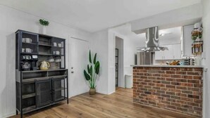 A modern kitchen with a brick accent wall, a black metal cabinet, and a hanging light fixture. - The Whimsy Retreat-amazing pool-5Brs-houston prime location Beltway 8 & US 69 (Houston)