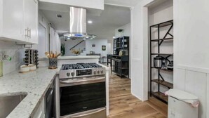 A modern kitchen with white cabinetry, a stainless steel range hood, and a wood floor. - The Whimsy Retreat-amazing pool-5Brs-houston prime location Beltway 8 & US 69 (Houston)