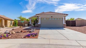 A residential house with a garage, a driveway, and a landscaped garden with rocks and purple flowers.