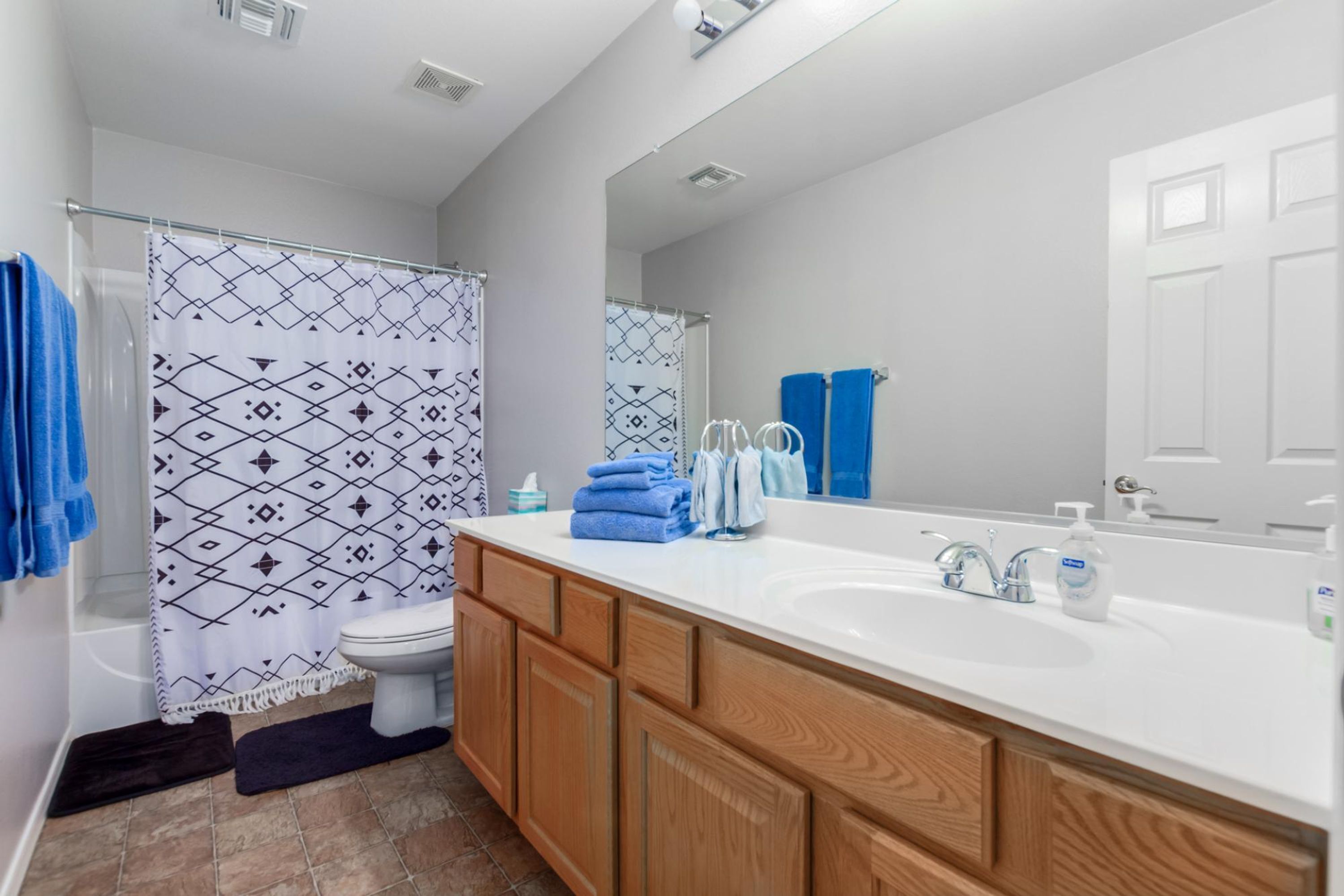 Un baño moderno con un lavamanos grande de color blanco, armarios de madera, un inodoro y una ducha con cortinas estampadas.