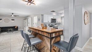 A modern kitchen with a central island, bar stools, and a dining area with a black sofa and coffee table. - Palm Tree Paradise Heated spa Pool Firepit (Glendale)
