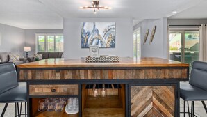 A modern kitchen with a wooden island, bar stools, and a large abstract painting on the wall. - Palm Tree Paradise Heated spa Pool Firepit (Glendale)