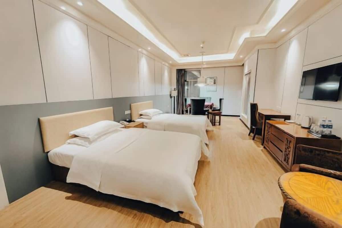 Ein Hotelzimmer mit zwei Betten, einem Schreibtisch, einem Stuhl, einem Fernseher und einer Küchenzeile.