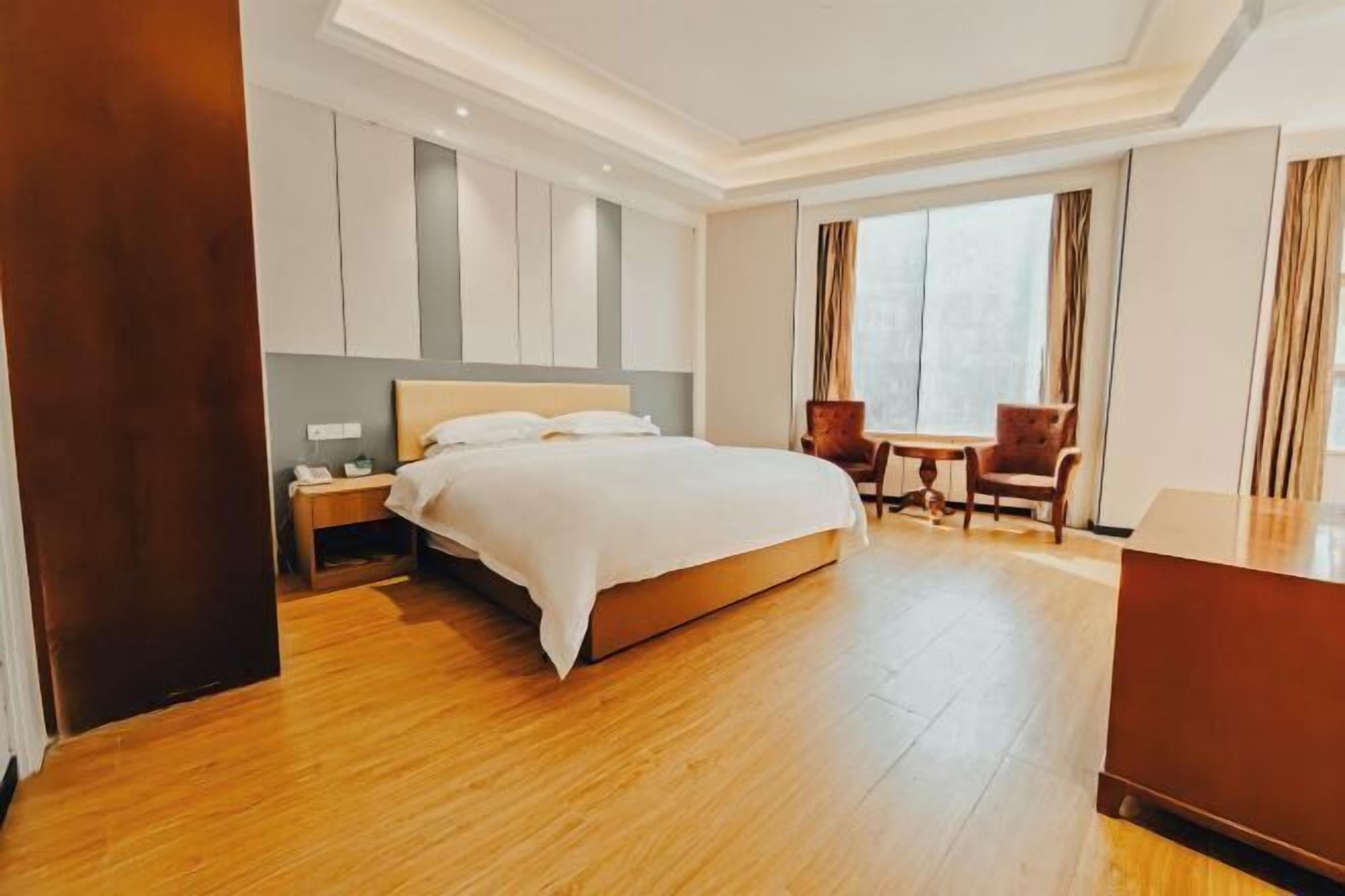 Een hotelkamer met een groot bed, een bureau, twee stoelen en een raam met gordijnen.