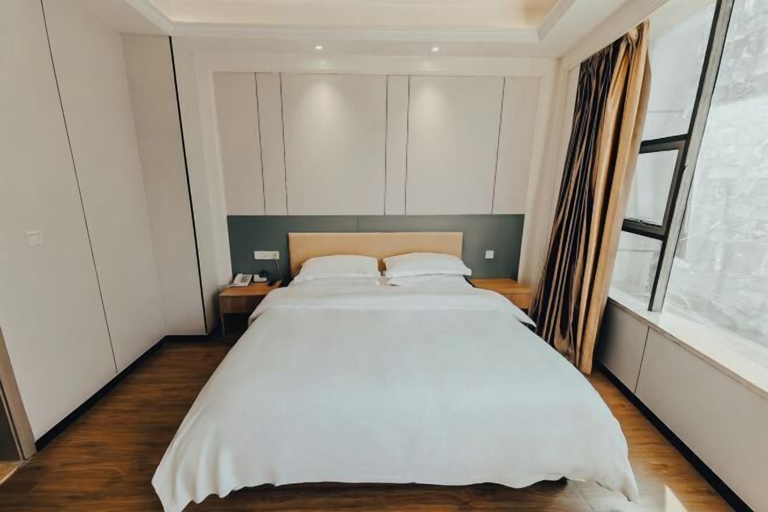Een moderne hotelkamer met een groot bed, houten vloeren, een nachtkastje en een raam met gordijnen.