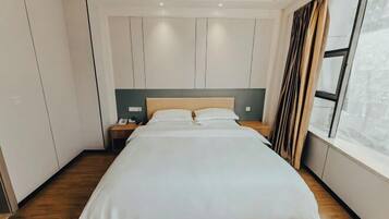 Een moderne hotelkamer met een groot bed, houten vloeren, een nachtkastje en een raam met gordijnen.