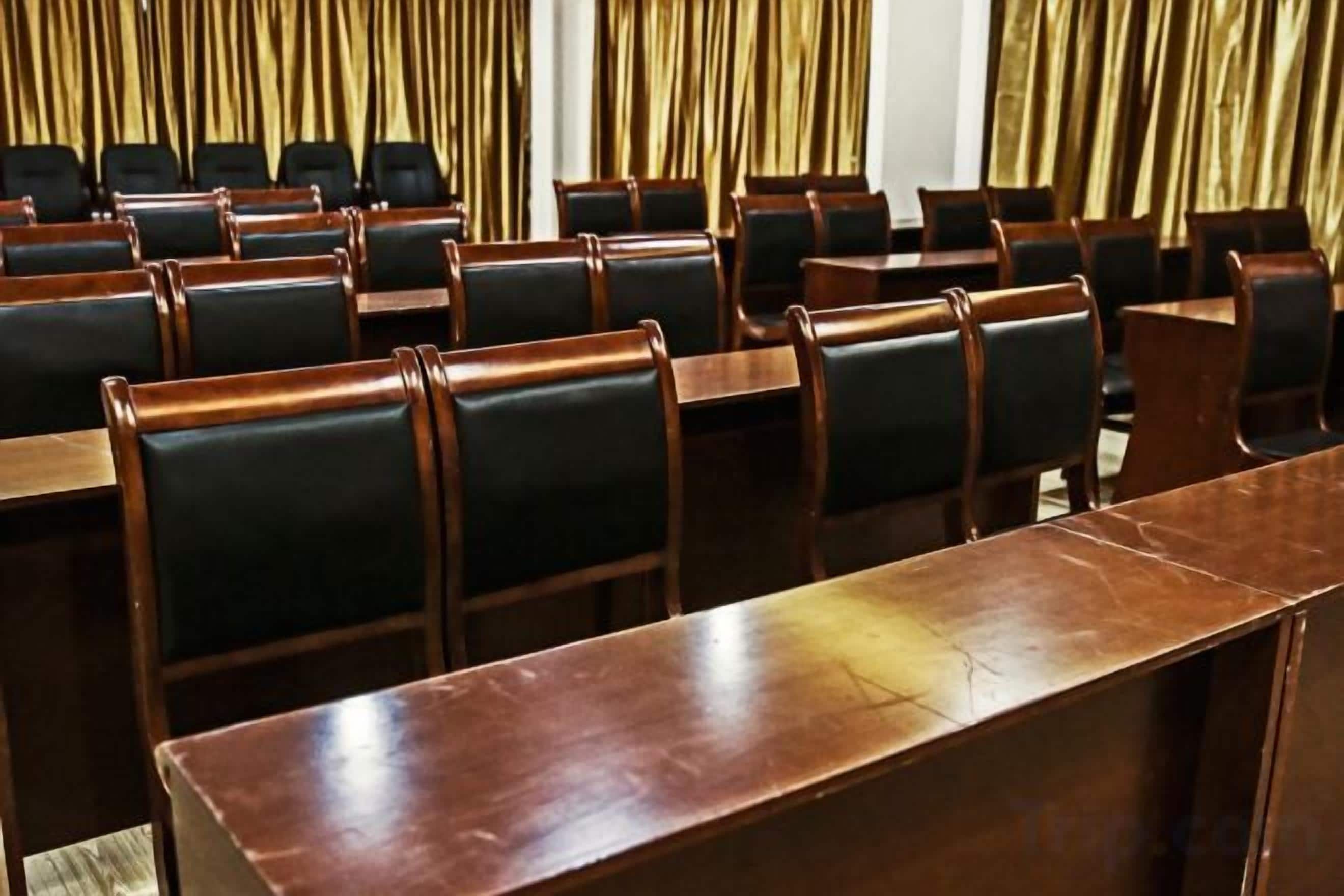 A conference room with rows of wooden tables and black chairs.