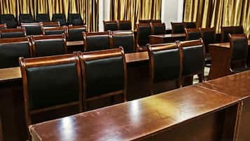 A conference room with rows of wooden tables and black chairs.