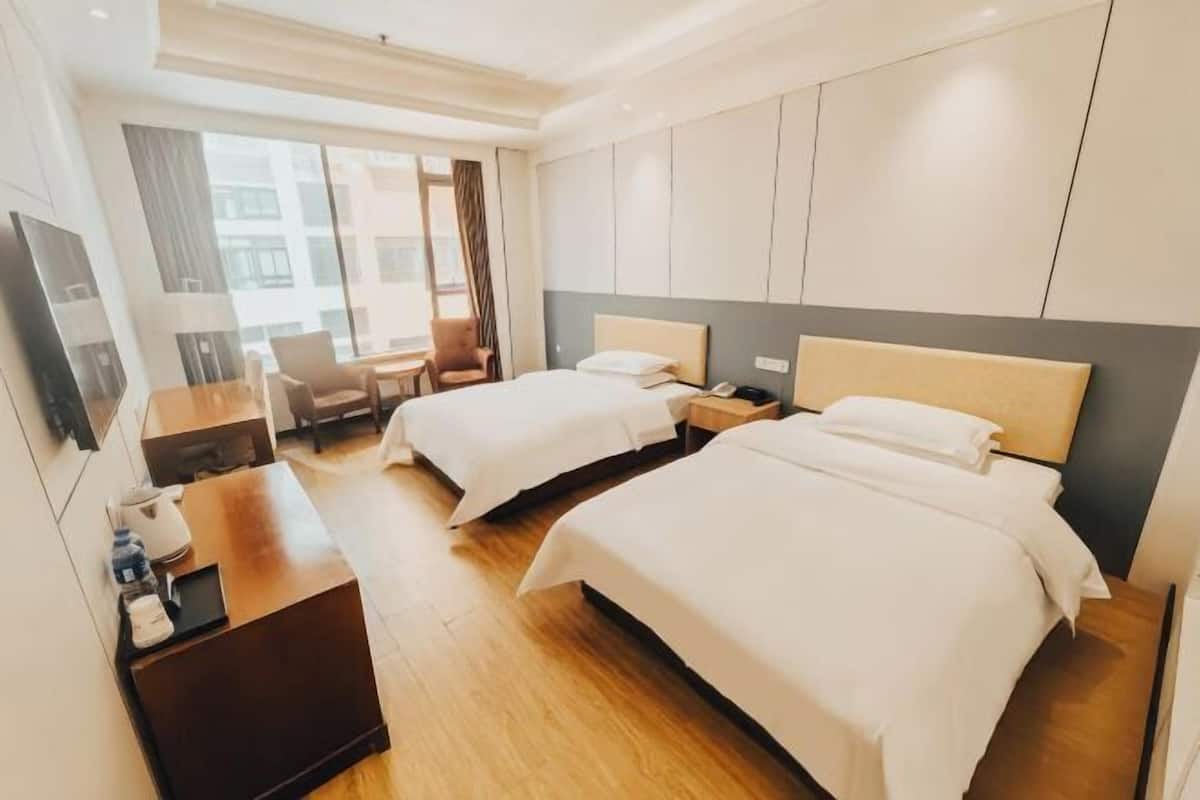 Ein Hotelzimmer mit zwei Betten, einem Schreibtisch, einem Stuhl, einem Fernseher und einem Fenster mit Vorhängen.