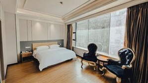 Ein Hotelzimmer mit einem Bett, einem Nachttisch, einem Sessel, einem kleinen Tisch und einem großen Fenster mit Vorhängen.