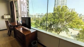 Una habitación con un ventanal grande, un escritorio de madera, un televisor y un cubo de basura.