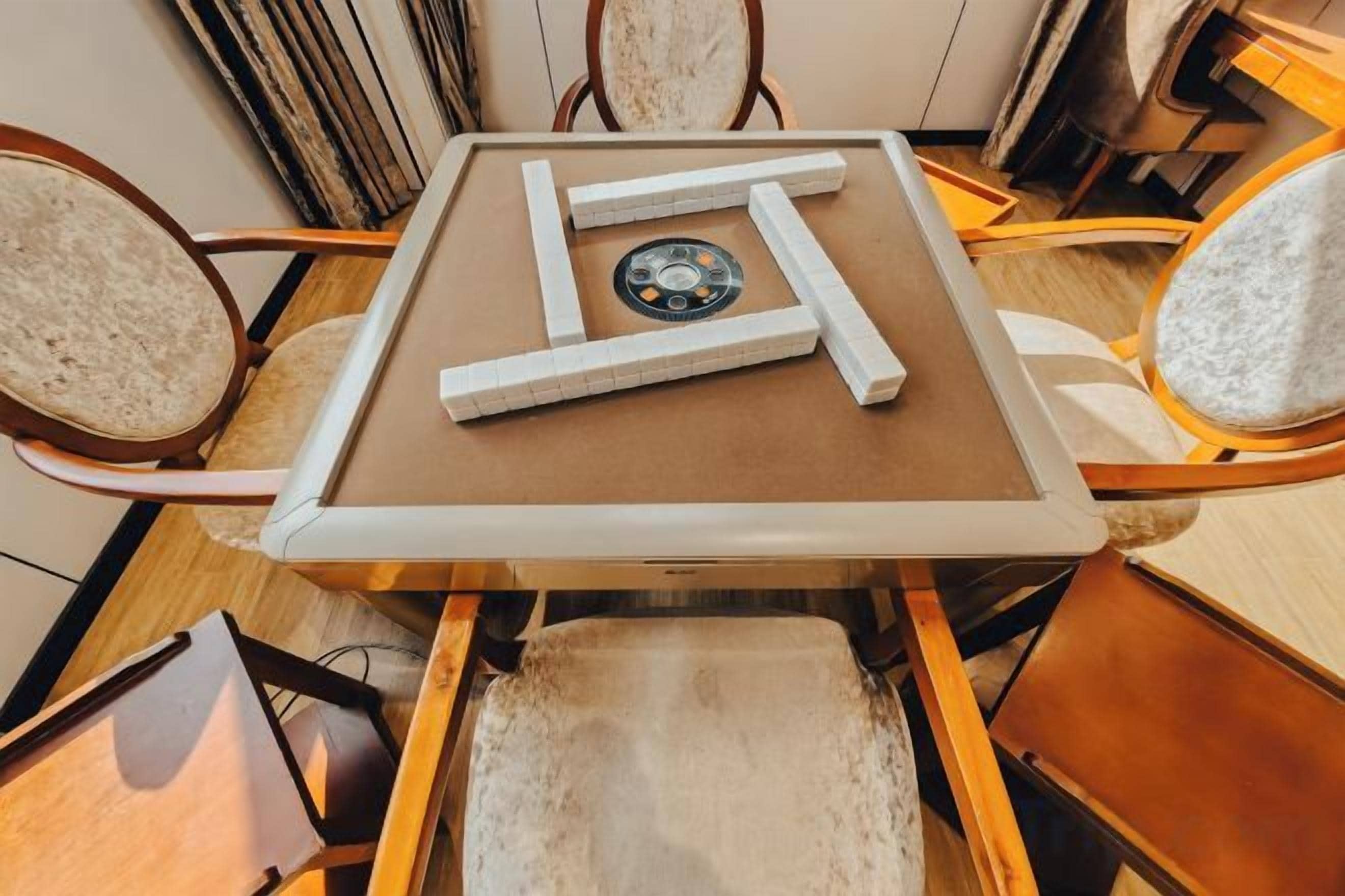 Una mesa cuadrada con superficie marrón y marco blanco, rodeada por cuatro sillas con cojines de color claro.