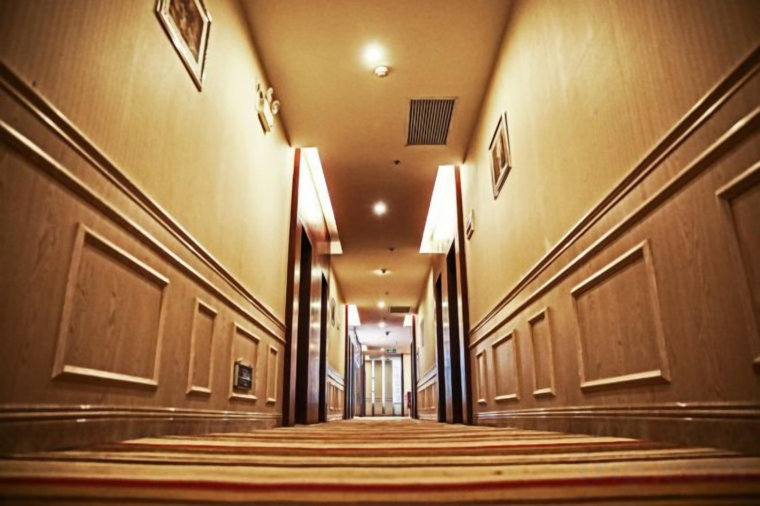 A hotel hallway with a carpeted floor, wooden paneling on the walls, and a series of doors along the corridor.