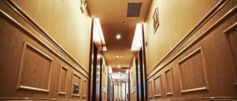 A hotel hallway with a carpeted floor, wooden paneling on the walls, and a series of doors along the corridor.