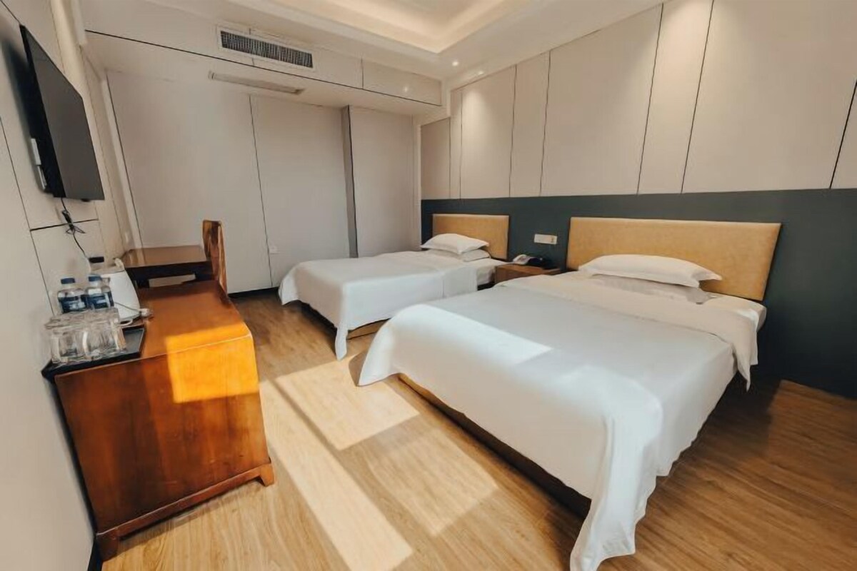 Habitación de hotel con dos camas, un escritorio de madera, un televisor y un armario.