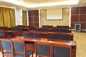 Ein Konferenzraum mit Reihen aus Holztischen und Stühlen, einer Projektionsleinwand und einem Präsentationsbildschirm.