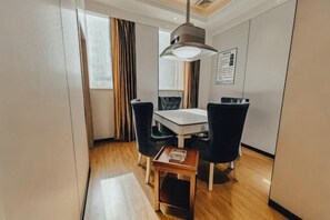 A modern hotel room with a wooden floor, a white table with four black chairs, a hanging light fixture, and a small wooden side table with a tray. - Haotai City Hotel (Jingzhou Renxinhui) (Jingzhou)
