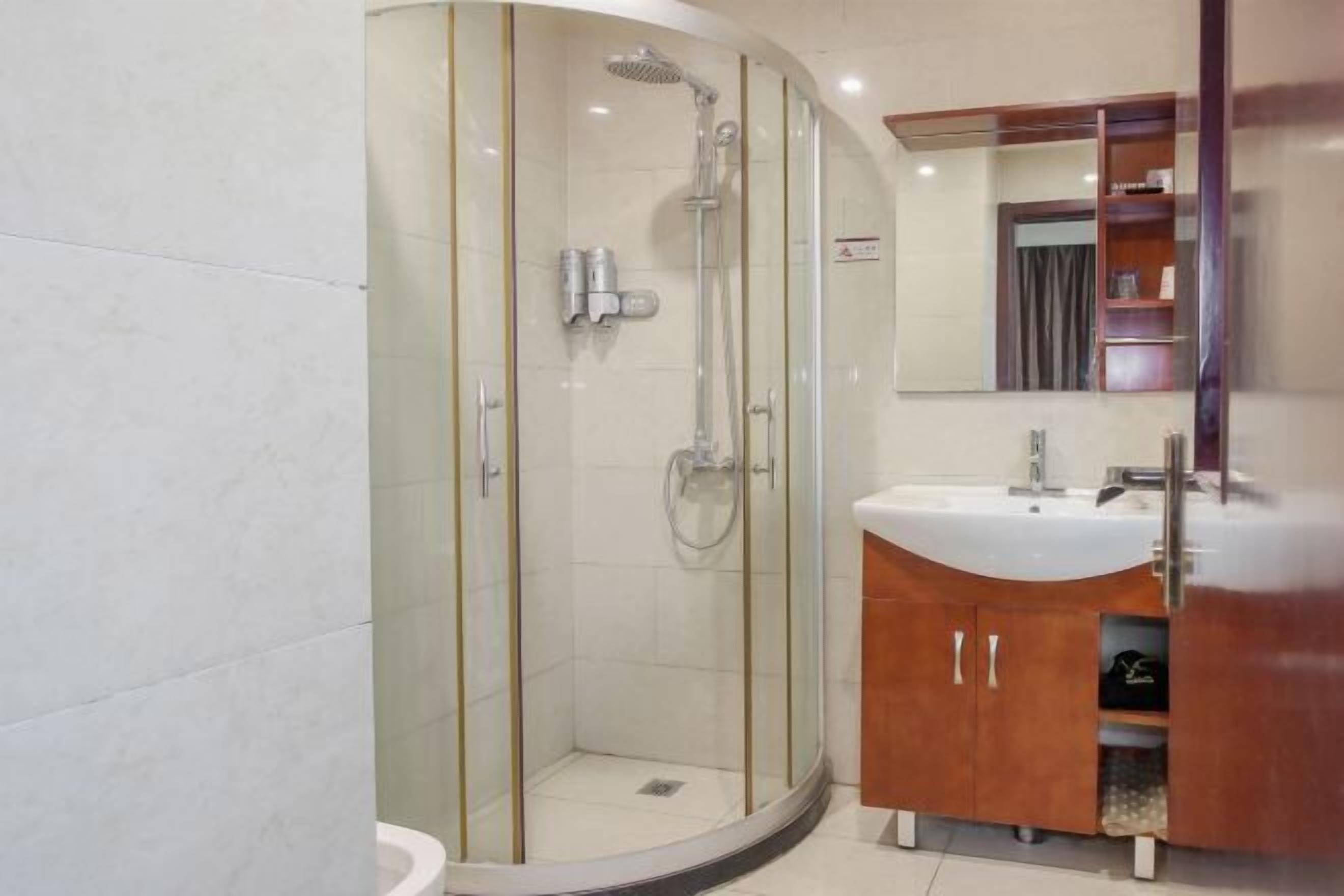 Een moderne badkamer met een douchecabine van glas, een witte wastafel en een houten opbergmeubel.