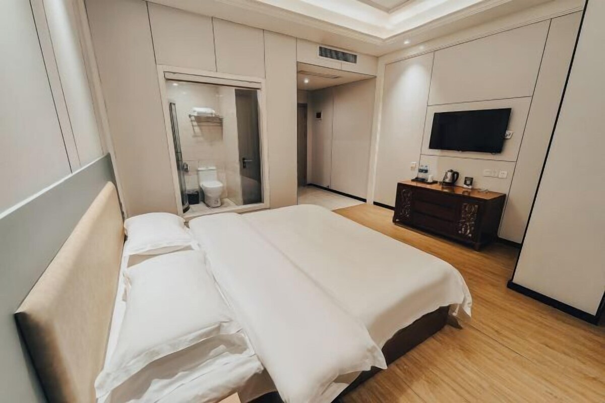 Une chambre d’hôtel avec un grand lit, un téléviseur fixé au mur et une salle de bain visible à travers une porte ouverte.
