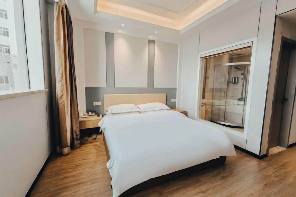 Ein modernes Hotelzimmer mit einem großen Bett, einem Nachttisch, einem Schreibtisch, einer Dusche mit Glastrennwand und Blick auf die Stadt.