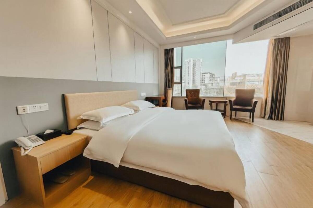 Ein Hotelzimmer mit Bett, Nachttisch, Stuhl und Blick auf die Stadt.