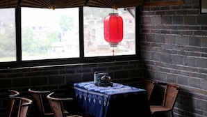 Una habitación de esquina con paredes de ladrillo, una mesa con mantel estampado, dos sillas de mimbre y un farol rojo.