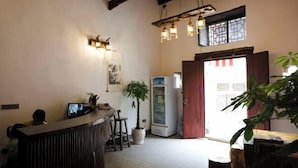 Zona de recepción con mostrador de madera, planta en maceta, refrigerador y puerta que da al exterior.