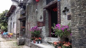 Un edificio tradicional de piedra con puerta de madera y escalones que conducen a un balcón. Hay plantas con flores en macetas sobre los escalones y una bicicleta estacionada afuera.