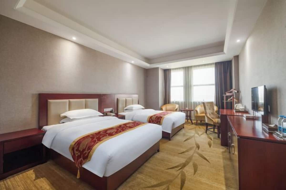 Une chambre d’hôtel avec deux lits, un bureau, une chaise, une télévision et une fenêtre avec des rideaux.