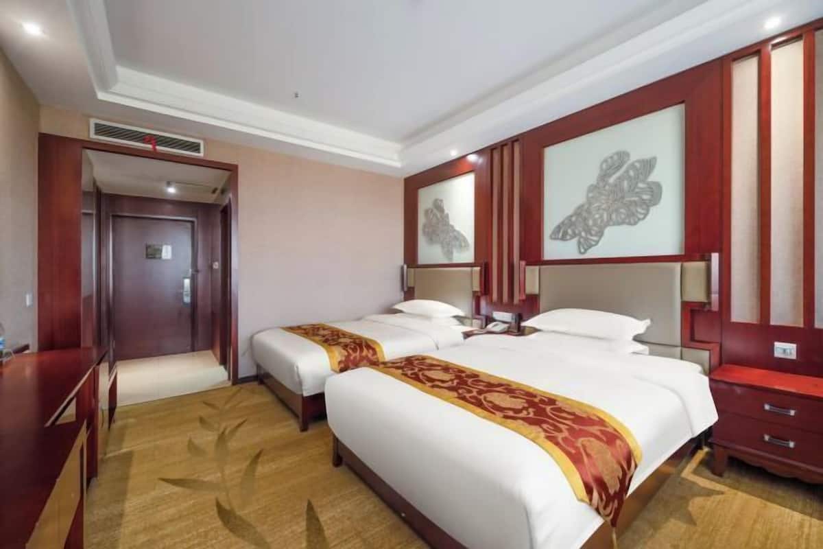 Une chambre d’hôtel avec deux lits, une commode en bois, un miroir et un panneau décoratif mural.