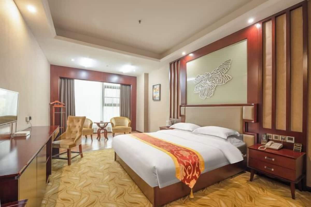 Une chambre d’hôtel avec un grand lit, un bureau, une chaise, une petite table et un élément décoratif mural.