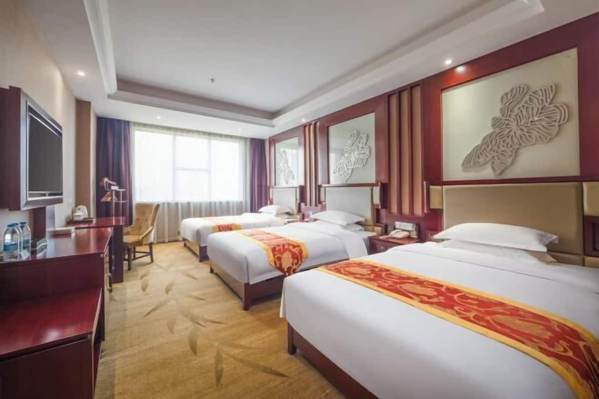 Une chambre d’hôtel avec trois lits, un bureau, une télévision et des panneaux décoratifs sur les murs.