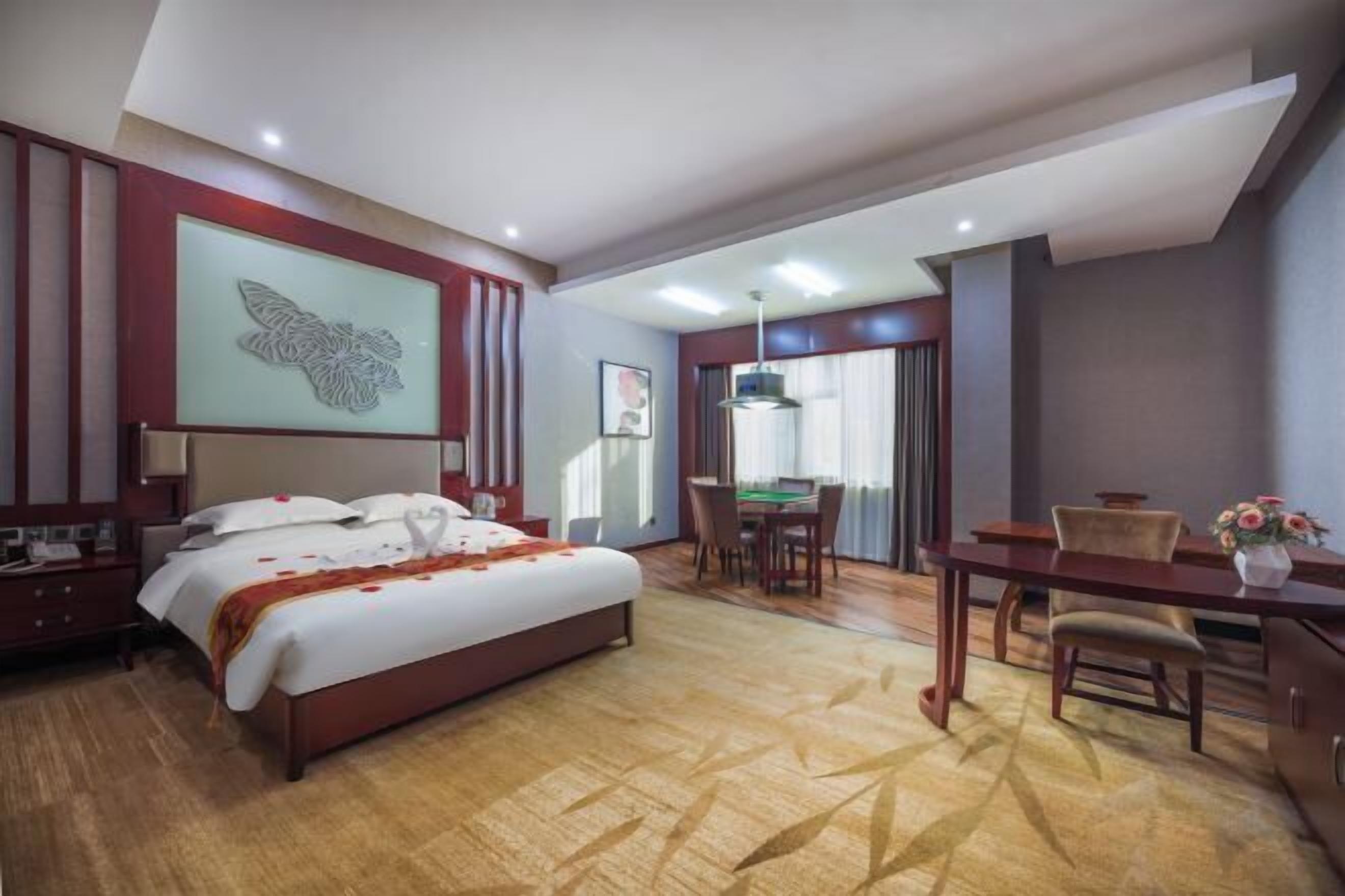 A hotel room with a large bed, a desk, and a dining area.