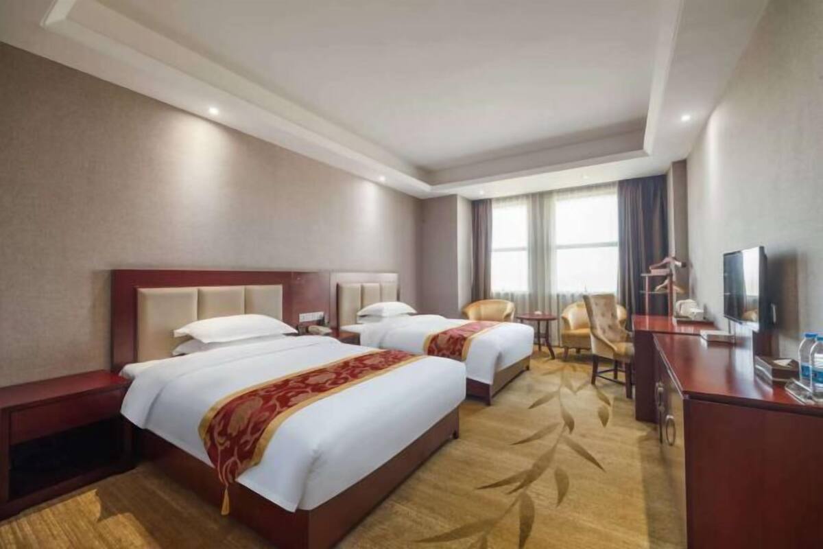 Une chambre d’hôtel avec deux lits, un bureau, une chaise, une télévision et une fenêtre avec des rideaux.