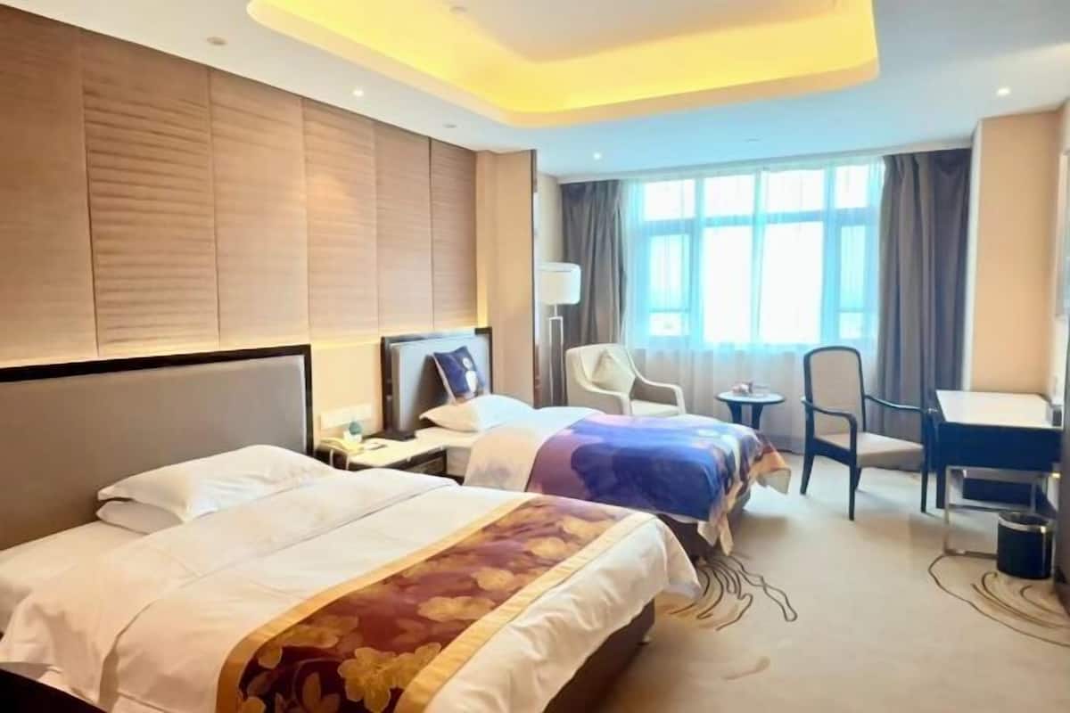 Une chambre d’hôtel avec deux lits, un bureau, une chaise et une fenêtre avec des rideaux.