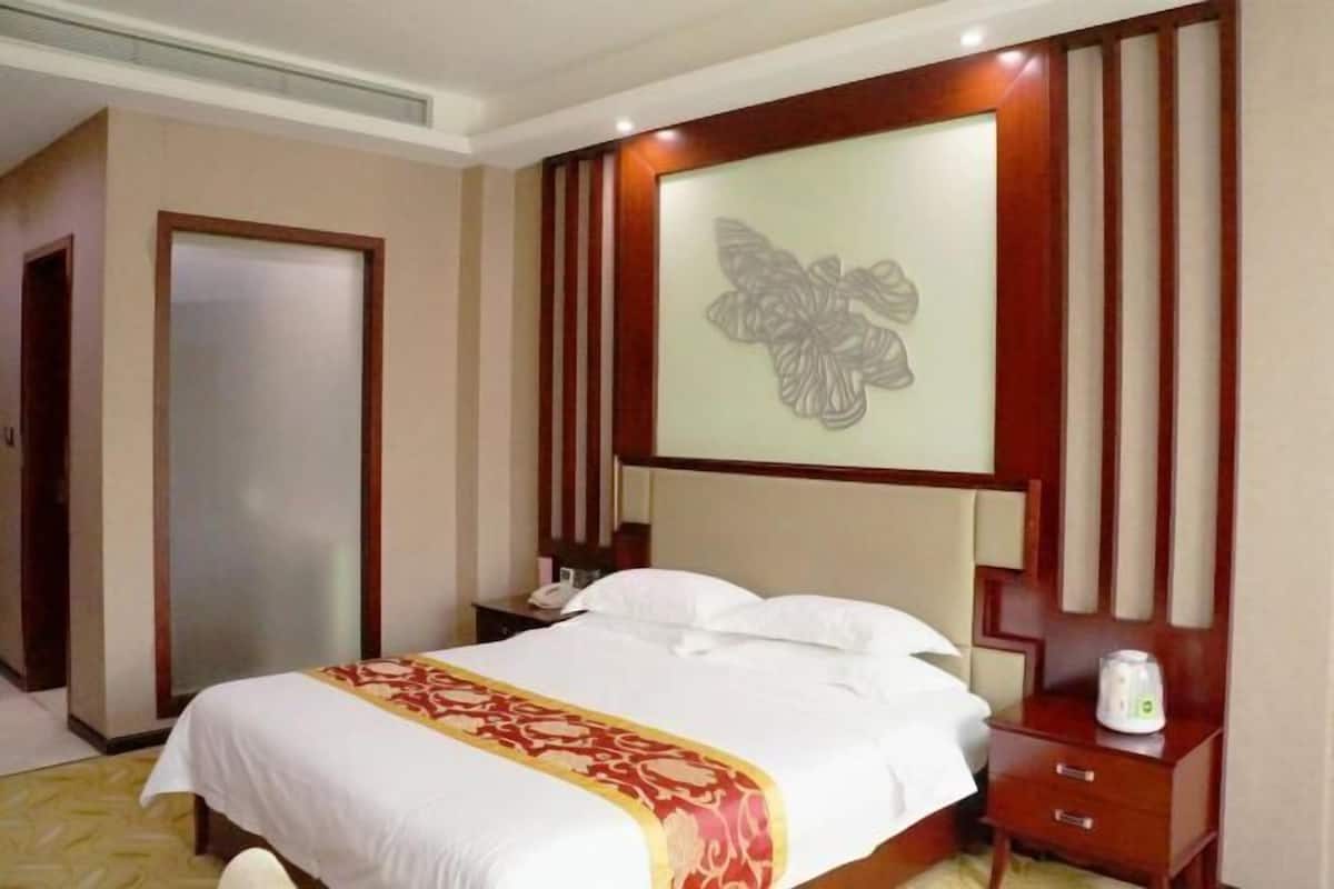 Une chambre d’hôtel comprenant un lit, une table de chevet, un panneau décoratif au mur et une porte.
